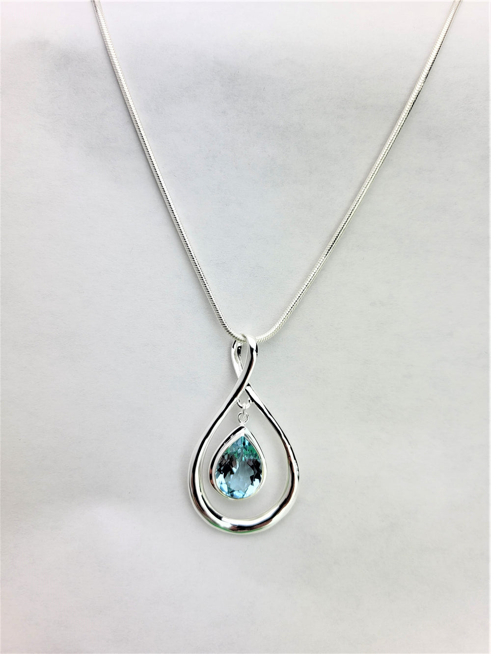 Behold our opulent sterling silver pear-shaped slide, embellished with a captivating 16mm x 12mm faceted light blue topaz. Meticulously crafted with .925 Sterling Silver, it flawlessly complements our 3mm Domed Omega Sterling Silver Necklace. Indulge in the ultimate expression of luxury and sophistication.