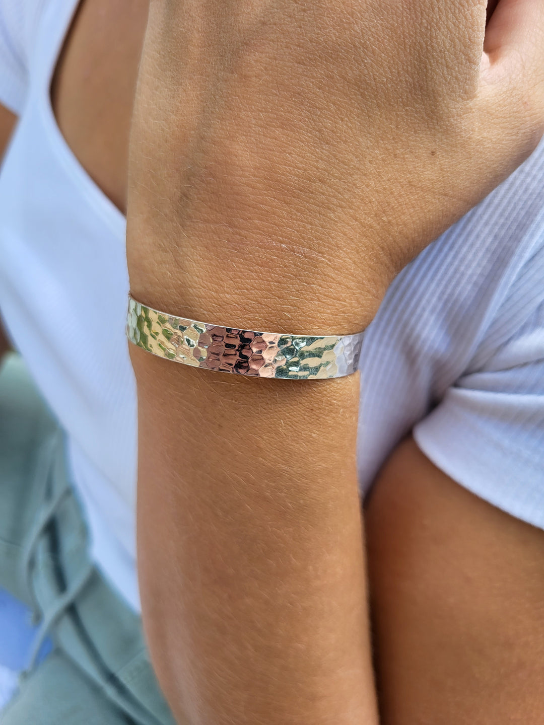 Close up outdoor image of woman wearing the hammered sterling silver cuff.