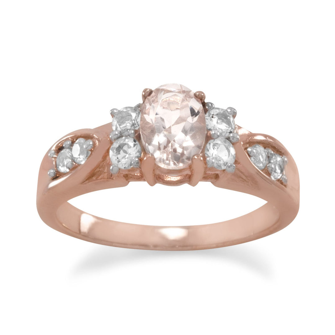 14 karat rose gold plated sterling silver ring with center 5mm x 7mm oval morganite and two 2.5mm white topaz on either side. The band graduates from 4.8mm - 2.2mm and is embellished with 2mm white topaz. This ring is available in whole sizes 5-9.